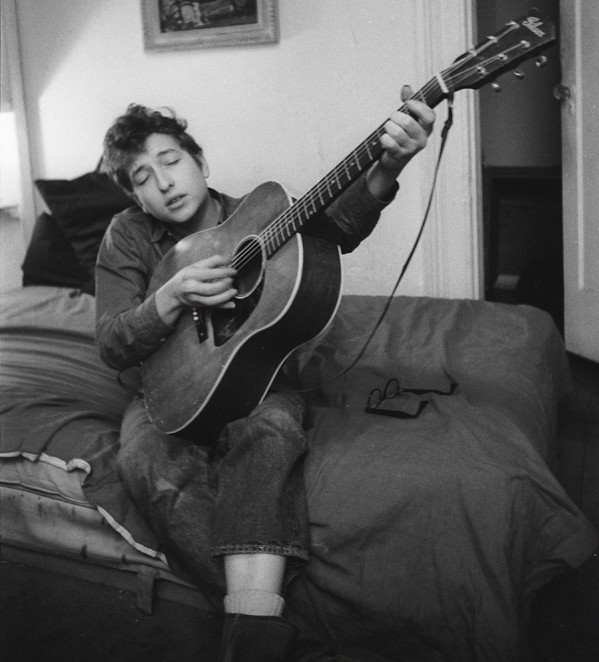 Bob Dylan playing guitar on his bed in his apartment, 161 W 4th St, Greenwich Village, NYC, 1961; © Ted Russell / Govinda Gallery | Bob Dylan, NYC 1961-64 – photographs by Ted Russell | Thursday 21 January – Sunday 21 February 2016 | Photo Museum Ireland