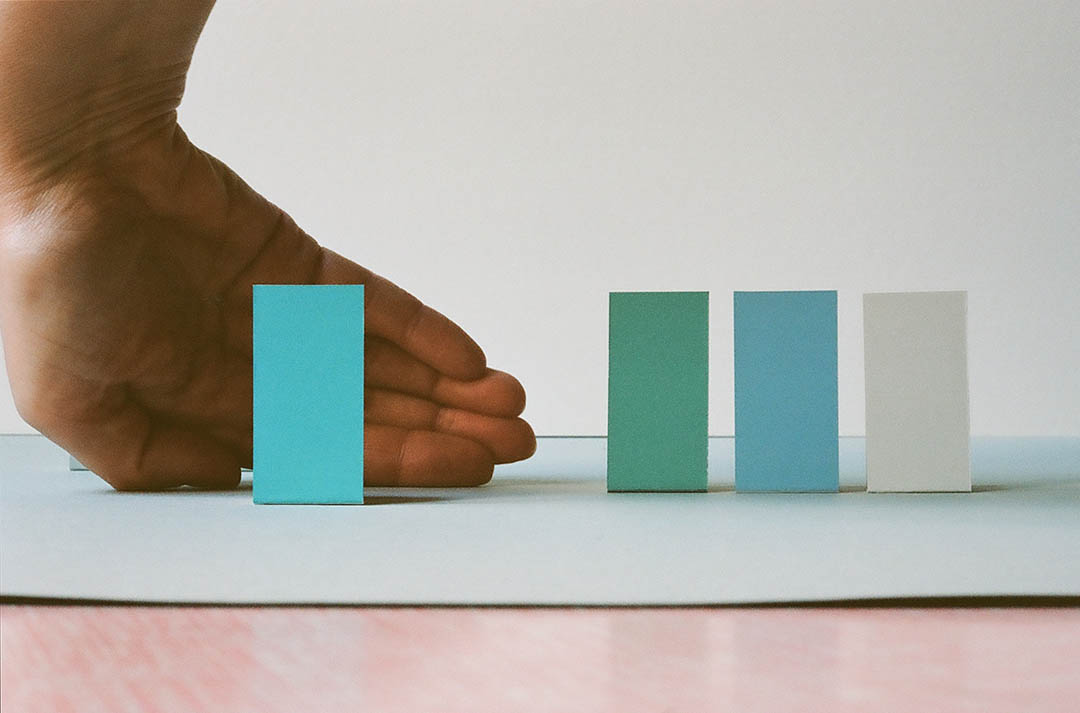 Irina Gheorghe, 2023 | Irina Gheorghe: Principles of Space Detection | Wednesday 1 March – Friday 31 March 2023 | NCAD Gallery | Image: Irina Gheorghe, 2023 – photo of four coloured strips of paper (?) standing proud from a flat surface; the wrist and palm of someone's right hand are visible towards the left, behind the leftmost, pale-blue strip 