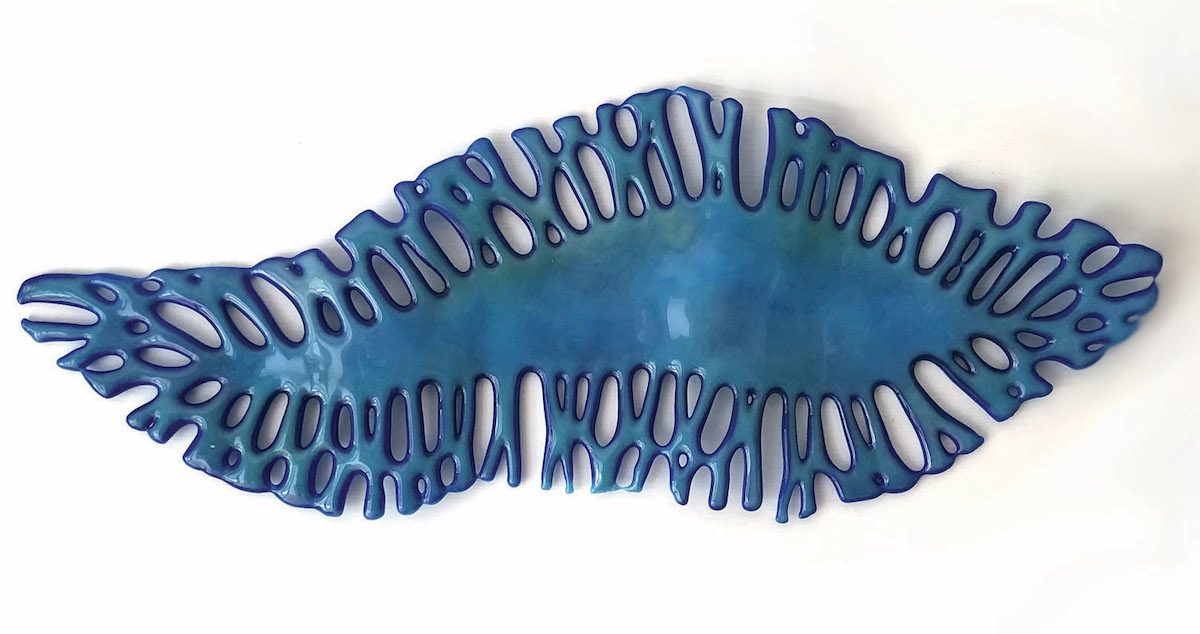 Trish Goodbody, Uisce, kiln-formed glass | Uillinn West Cork Arts Centre Members and Friends | Saturday 17 June – Thursday 20 July 2023 | Uillinn: West Cork Arts Centre | Image: Trish Goodbody, Uisce, kiln-formed glass – a fairly flat ceramic piece in shades of blue, with fronds of a sort emanating from a central body; suggestive of a sea creature 