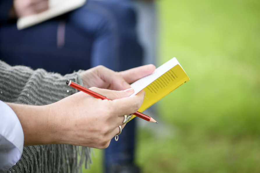 IMMA International Summer School 2023: Art and Politics #5 Assembly | Monday 19 June – Friday 30 June 2023 | IMMA | Image: photo of two hands holding a red pencil and a small yellow notebook in an outdoor setting – probably just a stock photo 