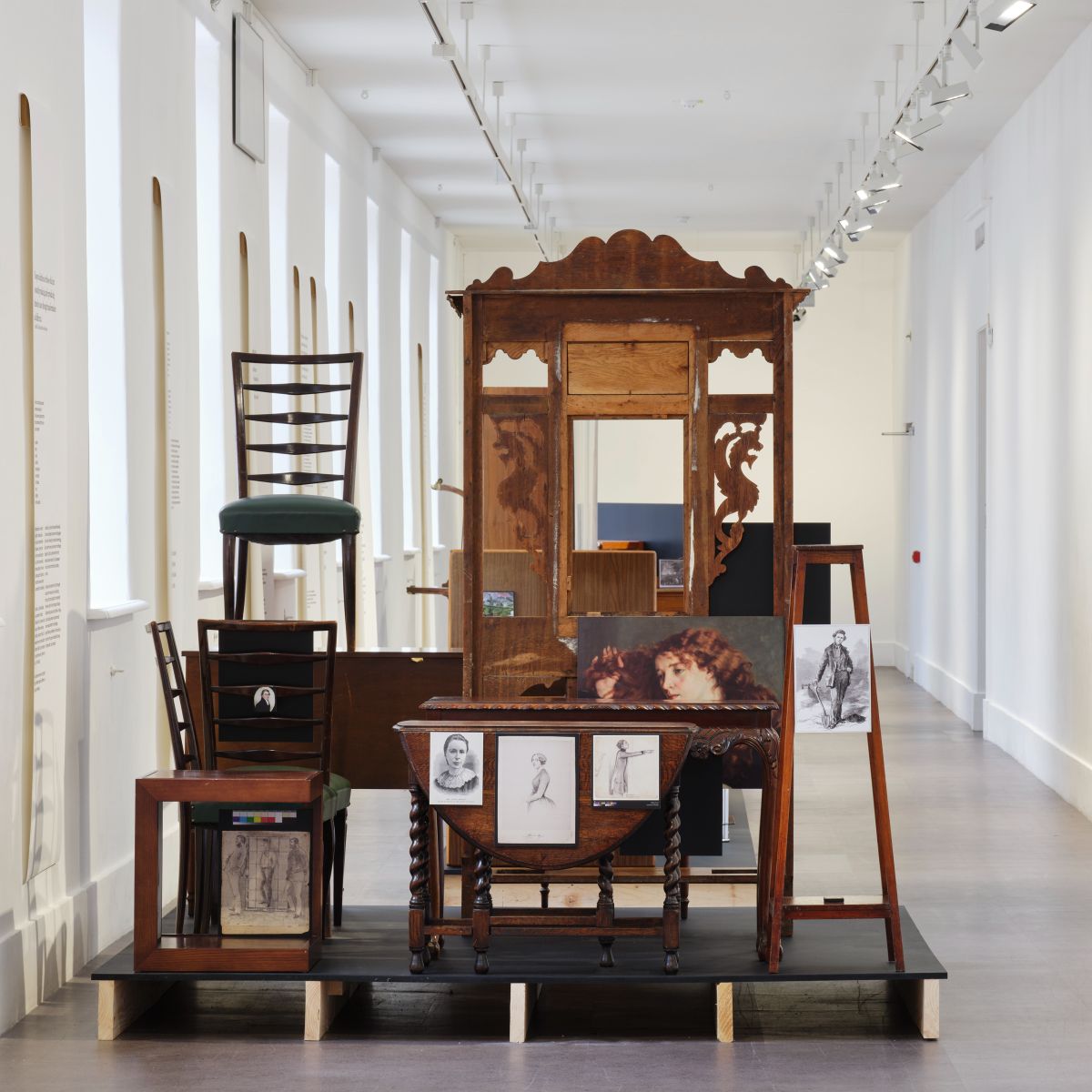 Sarah Pierce: Scene of the Myth Seminar & Finale Gathering | Saturday 2 September | IMMA | Image: photo of an installation in a corridor at IMMA; various pieces of furniture are arranged / stacked on a low improvised platform; there are chairs, a table or two, a hall stand with missing bits…; some images are attached to these pieces of furniture – e.g., stuck to the folded flap of a table – including a glimpse of Courbet’s painting ’Jo, la Belle Irlandaise’ 