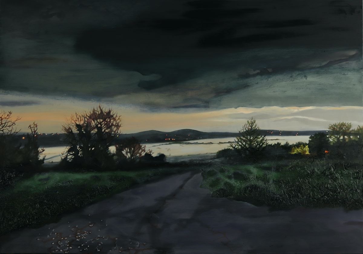 Ann Quinn: The Valley when the Mist is Strong, 2023, oil on panel, 70 x 100cm | Ann Quinn: Twilight Time | Friday 6 October – Saturday 28 October 2023 | Taylor Galleries | Image: Ann Quinn: The Valley when the Mist is Strong, 2023, oil on panel, 70 x 100cm | painting of a landscape at dusk; the mood is literally rather than figuratively dark; we’re looking down a road, more or less, towards what at first seems to be a lough or inlet, but must in fact be a valley covered in mist, as the title indicates – which explains the indications of walls or hedgerows poking out from an otherwise silky-white surface; closer to us are the shapes of trees / bushes in winter, one on the left perhaps a hawthorn; there are hills in the distance, an orange-ish tinge to the clouds towards the hidden horizon, and much darker clouds overhead 