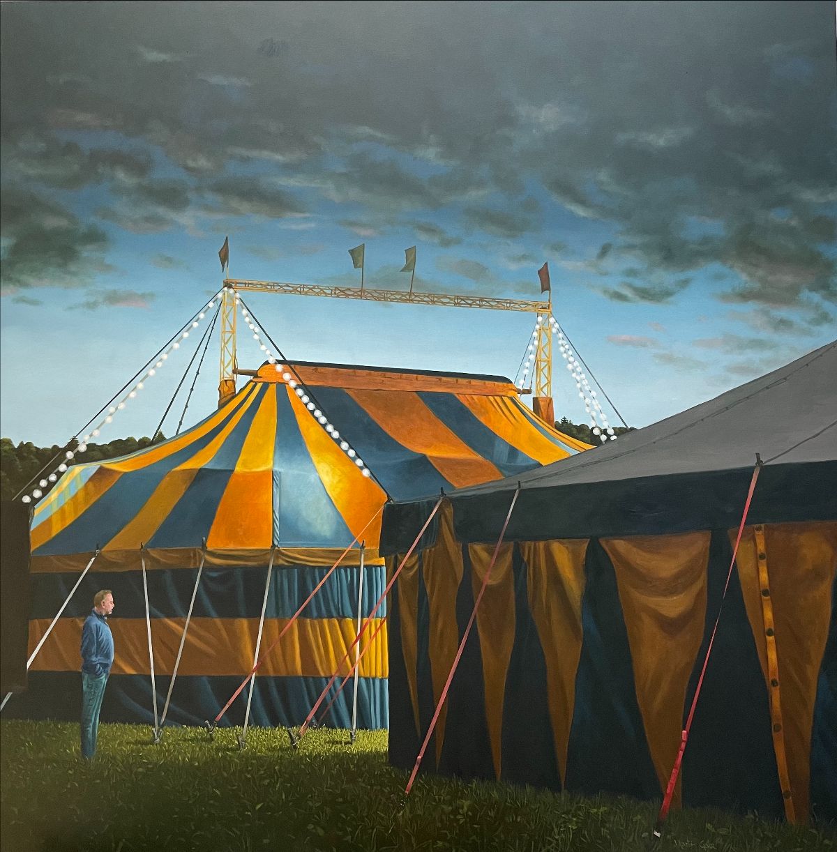 Martin Gale: Early Evening, 2022, oil on canvas, 120 x 120 cm | Martin Gale: HAPPENSTANCE | Friday 8 September – Saturday 30 September 2023 | Taylor Galleries | Image: Martin Gale: Early Evening, 2022, oil on canvas, 120 x 120 cm | the painting depicts partial views of two circus tents at twilight; the tents have broad stripes – some triangular – of orangey yellow and deepish-blue; guy ropes help hold up the tents; lit white lightbulbs are strung from the apices of the farther tent, which also sports various flags on a metalwork structure a man stands looking from the left side of the canvas into the gap between the two tents; there is a source of light in this gap 