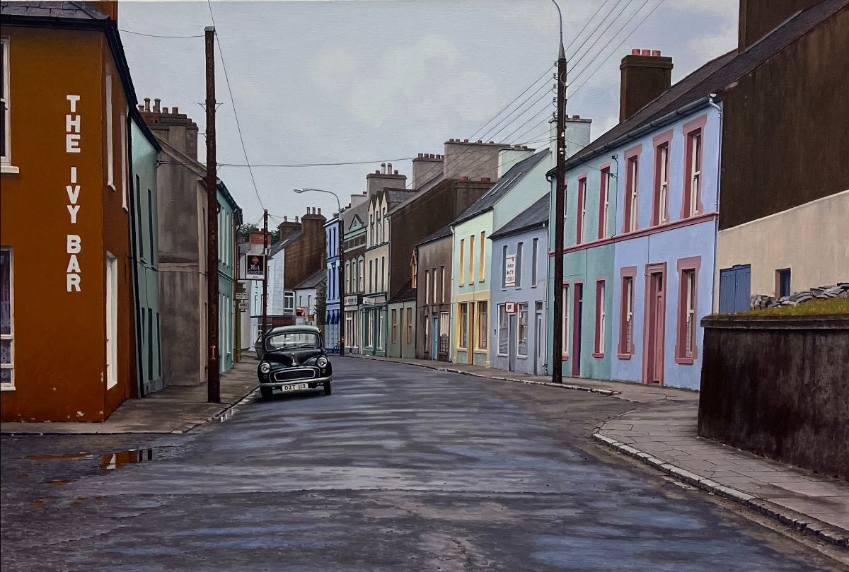 John Doherty: Winter Call Out, acrylic on linen, 81 x 122cm | John Doherty: Tempus Fugit et Vita Brevis | Friday 3 November – Saturday 25 November 2023 | Taylor Galleries | Image: John Doherty: Winter Call Out, acrylic on linen, 81 x 122cm | view of a largely residential street in a rural Irish town; the road is wet from a recent downpour; an old, black Morris Minor is the only car in the street; the corner of the nearest building on the left has written vertically on it ‘THE IVY BAR’ and in the distance down the street there seems to be a Guinness sign on another possible pub; there are tall wooden poles on either side of the street, presumably for phone and electricity; the sky is a pale, cloudy grey 