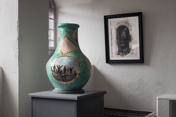 Spike Island Story | Alternative Ways of Seeing | Tuesday 19 March – Saturday 27 April 2024 | RUA RED | Image: Spike Island Story | photo; near the camera, a bit to the left in the image, is a vase on a grey pedestal; the vase is predominantly coloured turquoise, but there is a scene on it in a large vignette of what may be a protest or a victory of some sort; behind, on a wall, ther is a black-framed drawing of a black head; the room itself, painted grey, appears to be in an old building 