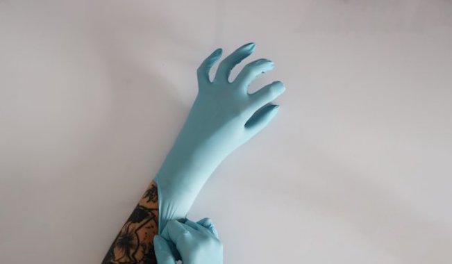 Chloe Austin: Living but a Day: Encounters | Friday 24 May – Tuesday 11 June 2024 | The LAB | Image: photo of a tattooed forearm onto which a pale-blue rubber glove is being pulled by another pale-blue rubber-gloved hand 