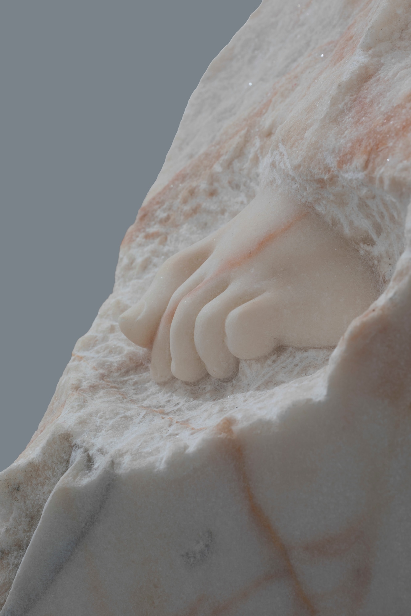 Dorothy Cross: Tread (detail), 2023, hand-carved marble, dimensions variable, https://dnote.website/wordpres2/wp-content/uploads/2024/05/veins-of-other-cross-375x375.jpeg | Dorothy Cross: Veins of Other | Friday 24 May – Saturday 6 July 2024 | Kerlin Gallery | Image: Dorothy Cross: Tread (detail), 2023, hand-carved marble, dimensions variable | photo of a sculpture in marble; we see not much more than the toes of what may be a child’s foot sticking out of otherwise unchiselled marble; the marble has orange veins running through it 