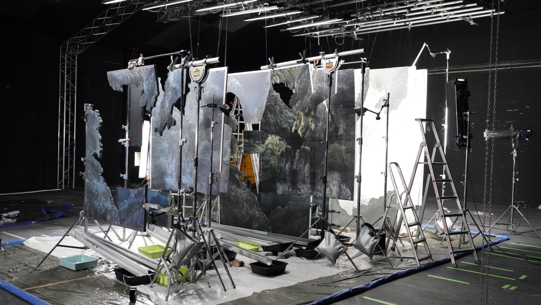 Noémie Goudal, behind the scenes of Supra Strata, 2024, courtesy of the artist and Edel Assanti, London | Noémie Goudal: Tilt | Saturday 10 May – Saturday 2 August 2025 | The Dock | Image: Noémie Goudal, behind the scenes of Supra Strata, 2024, courtesy of the artist and Edel Assanti, London | photo showing a series of ‘canvases’ – pieces of material, often with large parts missing – hanging down from supports, one behind the other, such that someone looking from in front of the arrangement would see a series of layers, most pierced to reveal a further background behind; lighting is from above, and the space itself is painted black Noémie Goudal, behind the scenes of Supra Strata, 2024, courtesy of the artist and Edel Assanti, London | Noémie Goudal: Tilt | Saturday 10 May – Saturday 2 August 2025 | The Dock | Image: Noémie Goudal, behind the scenes of Supra Strata, 2024, courtesy of the artist and Edel Assanti, London | photo showing a series of ‘canvases’ – pieces of material, often with large parts missing – hanging down from supports, one behind the other, such that someone looking from in front of the arrangement would see a series of layers, most pierced to reveal a further background behind; lighting is from above, and the space itself is painted black