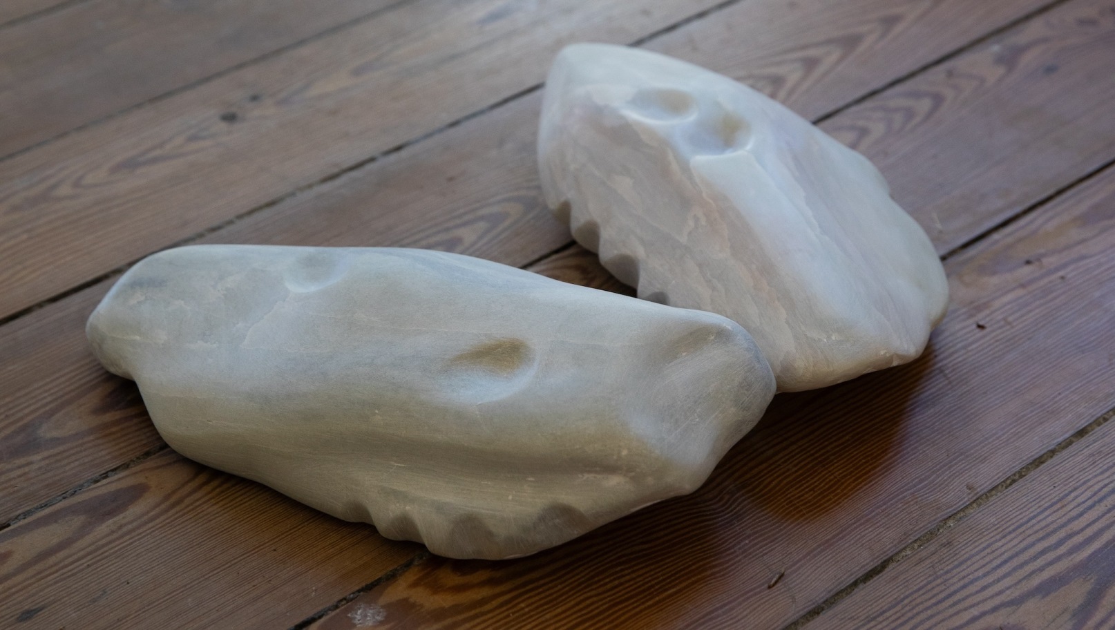 Marie Farrington: Diagonal Acts | Saturday 23 August – Saturday 1 November 2025 | The Dock | Image: photo of what looks like two pale stones with slight marbling; but they have curving shapes that resemble teeth, and pits that may also be manufactured; they are resting on a wooden surface of laths 