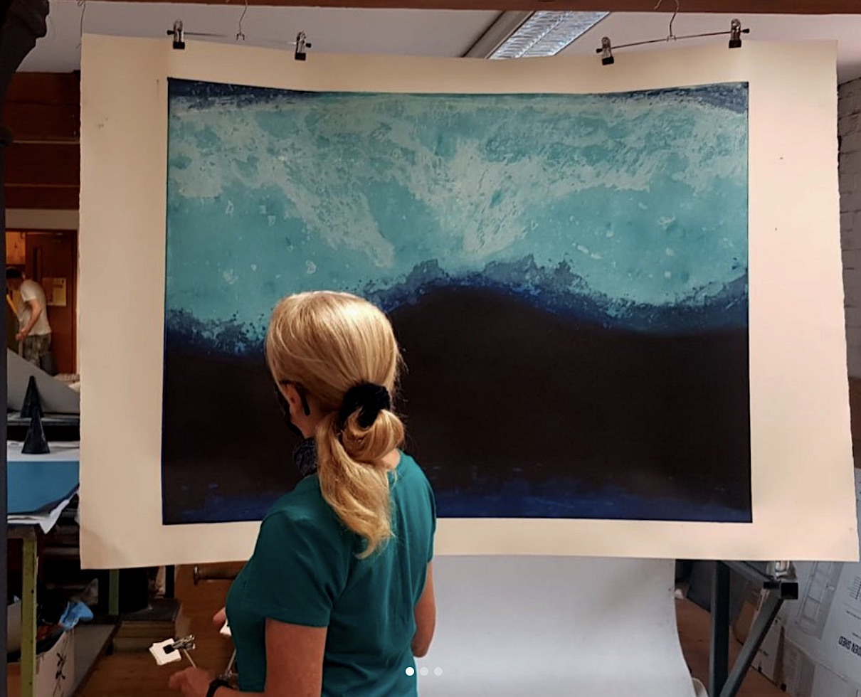 Gwen O'Dowd, pictured with her carborundum, Limen II | MÓR, 2023 | Saturday 22 April  – Saturday 3 June 2023 | Graphic Studio Gallery | Image: Gwen O'Dowd, pictured with her carborundum, Limen II – photo of the artist facing away from the camera, looking at a large carborundum print depicting what looks like a breaking wave 
