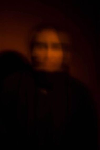Ala Buisir: Tint of Trauma | Friday 7 July  – Monday 31 July 2023 | Rua Red | Image: Khoula (pseudonym) by Ala Buisir – a very blurred image of a woman, in black and burnt-sienna tones; her face is lit, but otherwise the photo is dark to black 