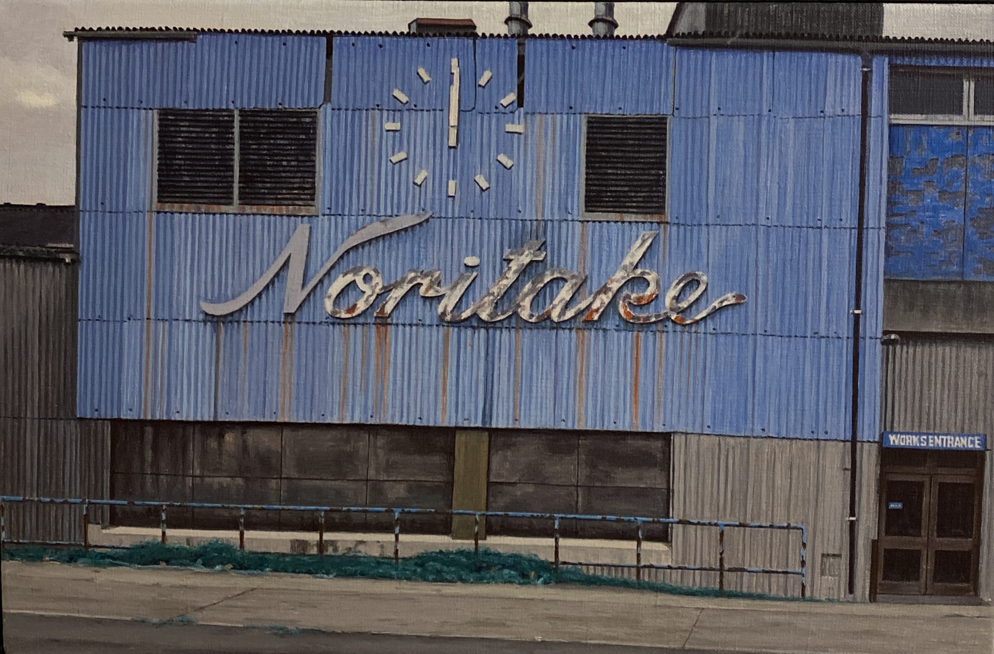 John Doherty: Noritake, Arklow Harbour, acrylic on canvas, 32 x 56cm | Summer Group Show – Gallery + Invited Artists | Monday 24 July  – Thursday 31 August 2023 | Taylor Galleries | Image: John Doherty: Noritake, Arklow Harbour, acrylic on canvas, 32 x 56cm – photo-realist painting of what was probably a factory; the façade is mostly pale-blue corrugated-iron sheeting, on top of which are a large clock (just rectangular ticks for the hours and longer rectangles for the hour and minute hands; all in faded white) and ‘Noritake’ in cursive stroke; there are what were probably windows at the bottom, filled with concrete blocks; there's a railing to the front; towards the right edge of the painting we see a 'Workers Entrance' sign above a pair of doors; there's a railing to the front, and suggestions of a footpath and road; the sky is grey.