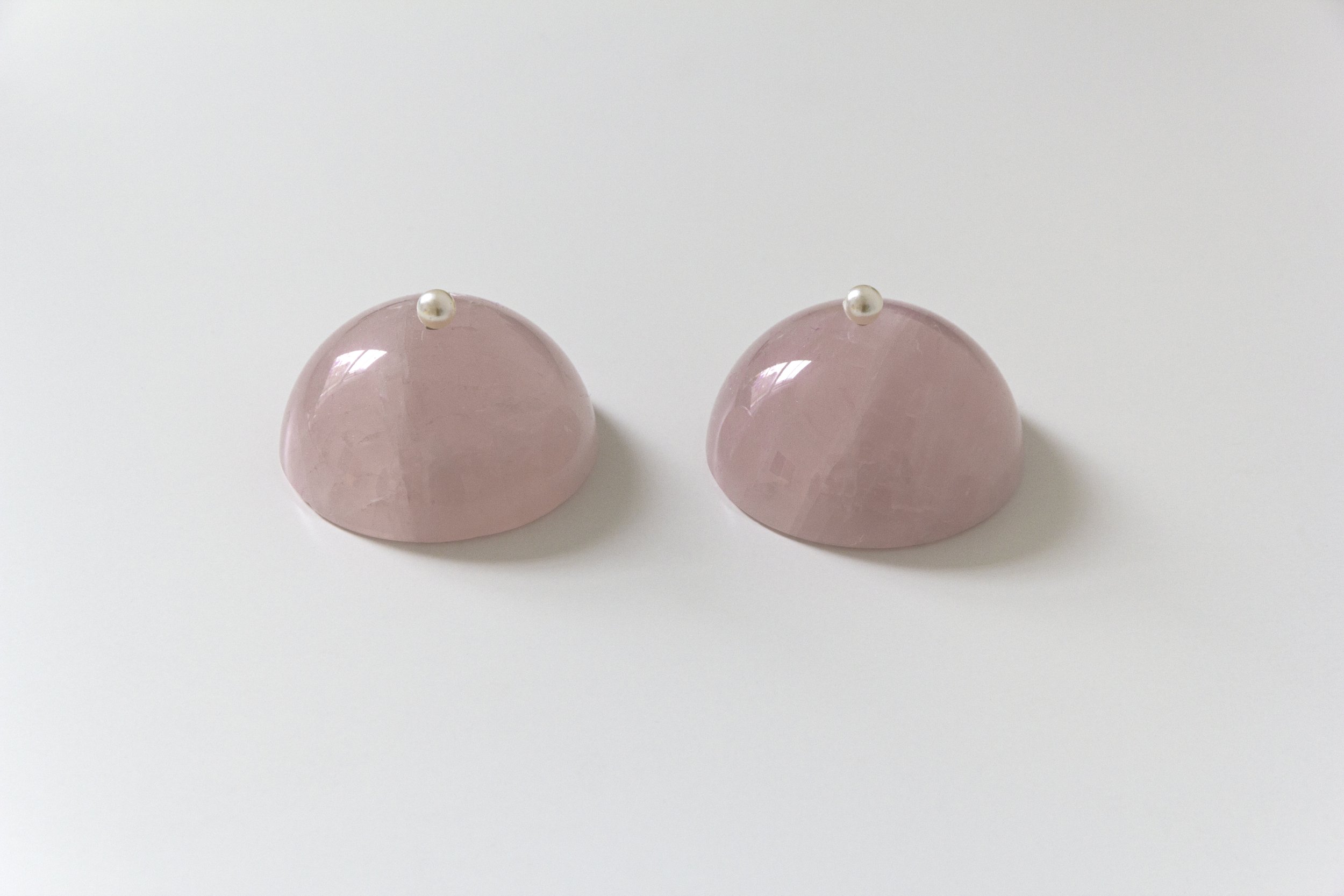 Kiera O’Toole, St. Agatha or Disco Tits | Karen Donnellan: Cosmic Wetness | Friday 25 August  – Sunday 1 October 2023 | Royal Hibernian Academy | Image: Kiera O’Toole, St. Agatha or Disco Tits – two ‘breasts’ side by side, with gap between them, against a whitish background and viewed from above and to the front; the breasts appear to be made of something pinkish (apart from pearl-like white or silver nipples) and glass-like; there are reflections of a window in the glass-like surfaces; this artwork may be a painting, though the shadows cast by the breasts suggest that it’s a photograph  