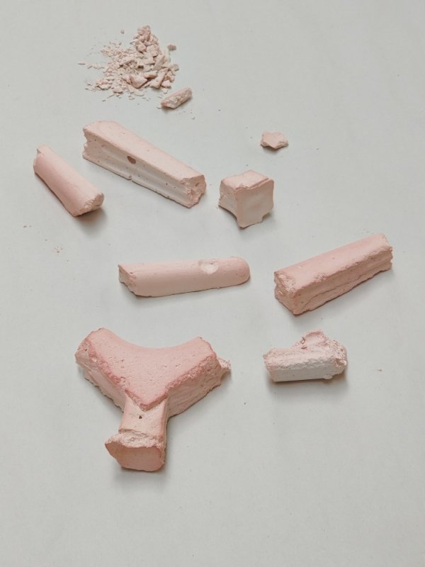 Elaine Granger: HOLDING ON lightly | Friday 15 September  – Monday 4 December 2023 | The LAB | Image: photo of what looks like broken pieces of pink plaster, arranged, though fairly randomly, with a little pile of plaster rubble farthest from us, at the top of the photo; the background, presumably a flat surface, is light grey, and an even light is coming primarily from above 