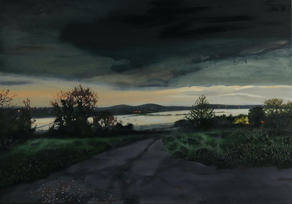 Ann Quinn: The Valley when the Mist is Strong, 2023, oil on panel, 70 x 100cm | Ann Quinn: Twilight Time | Friday 6 October  – Saturday 28 October 2023 | Taylor Galleries | Image: Ann Quinn: The Valley when the Mist is Strong, 2023, oil on panel, 70 x 100cm | painting of a landscape at dusk; the mood is literally rather than figuratively dark; we’re looking down a road, more or less, towards what at first seems to be a lough or inlet, but must in fact be a valley covered in mist, as the title indicates – which explains the indications of walls or hedgerows poking out from an otherwise silky-white surface; closer to us are the shapes of trees / bushes in winter, one on the left perhaps a hawthorn; there are hills in the distance, an orange-ish tinge to the clouds towards the hidden horizon, and much darker clouds overhead 