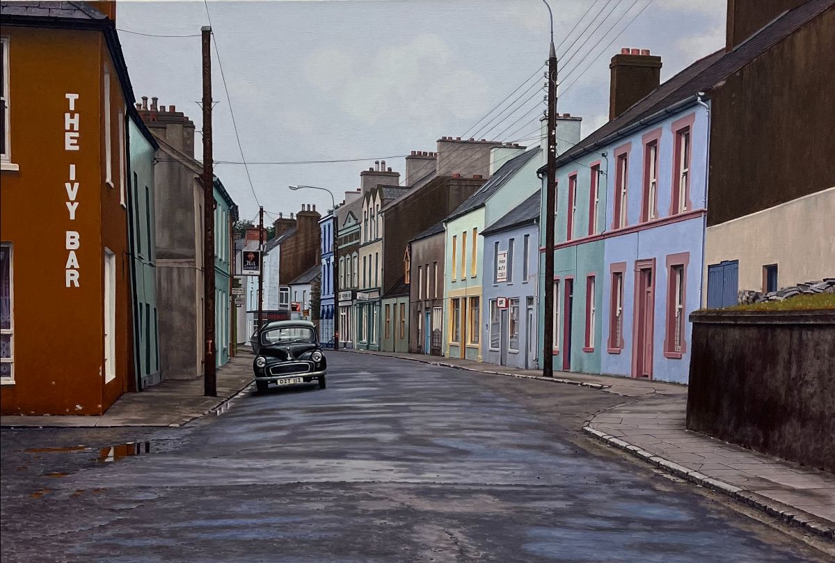 John Doherty: Winter Call Out, acrylic on linen, 81 x 122cm | John Doherty: Tempus Fugit et Vita Brevis | Friday 3 November  – Saturday 25 November 2023 | Taylor Galleries | Image: John Doherty: Winter Call Out, acrylic on linen, 81 x 122cm | view of a largely residential street in a rural Irish town; the road is wet from a recent downpour; an old, black Morris Minor is the only car in the street; the corner of the nearest building on the left has written vertically on it ‘THE IVY BAR’ and in the distance down the street there seems to be a Guinness sign on another possible pub; there are tall wooden poles on either side of the street, presumably for phone and electricity; the sky is a pale, cloudy grey 