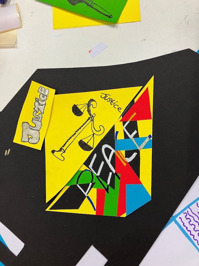 Justice + Peace – Youth Arts Exhibition | Saturday 9 December 2023  – Sunday 25 February 2024 | Municipal Gallery | Image: photo possibly of a work in progress; we see a collage on a black background that appears to have parts cut out of it, including a large area top-left in a curve; three pieces of yellow paper have been pasted onto the black; one to the left has ‘Justice’ written on it in what may be silver with the letters outlined in black; the second piece is a triangle, with a ‘scales of justice’ motif and the word ‘Justice’ at the top in black; the third piece of yellow paper has other, smaller pieces of coloured paper pasted onto it – black, red, green, blue, and the word ‘PEACE’ is written across them in black and white 
