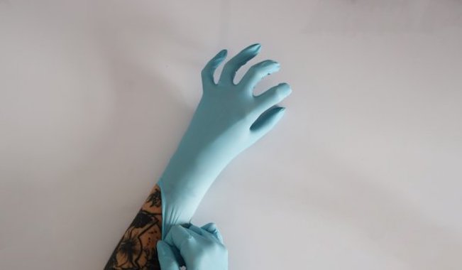 Chloe Austin: Living but a Day: Encounters | Friday 24 May  – Tuesday 11 June 2024 | The LAB | Image: photo of a tattooed forearm onto which a pale-blue rubber glove is being pulled by another pale-blue rubber-gloved hand 