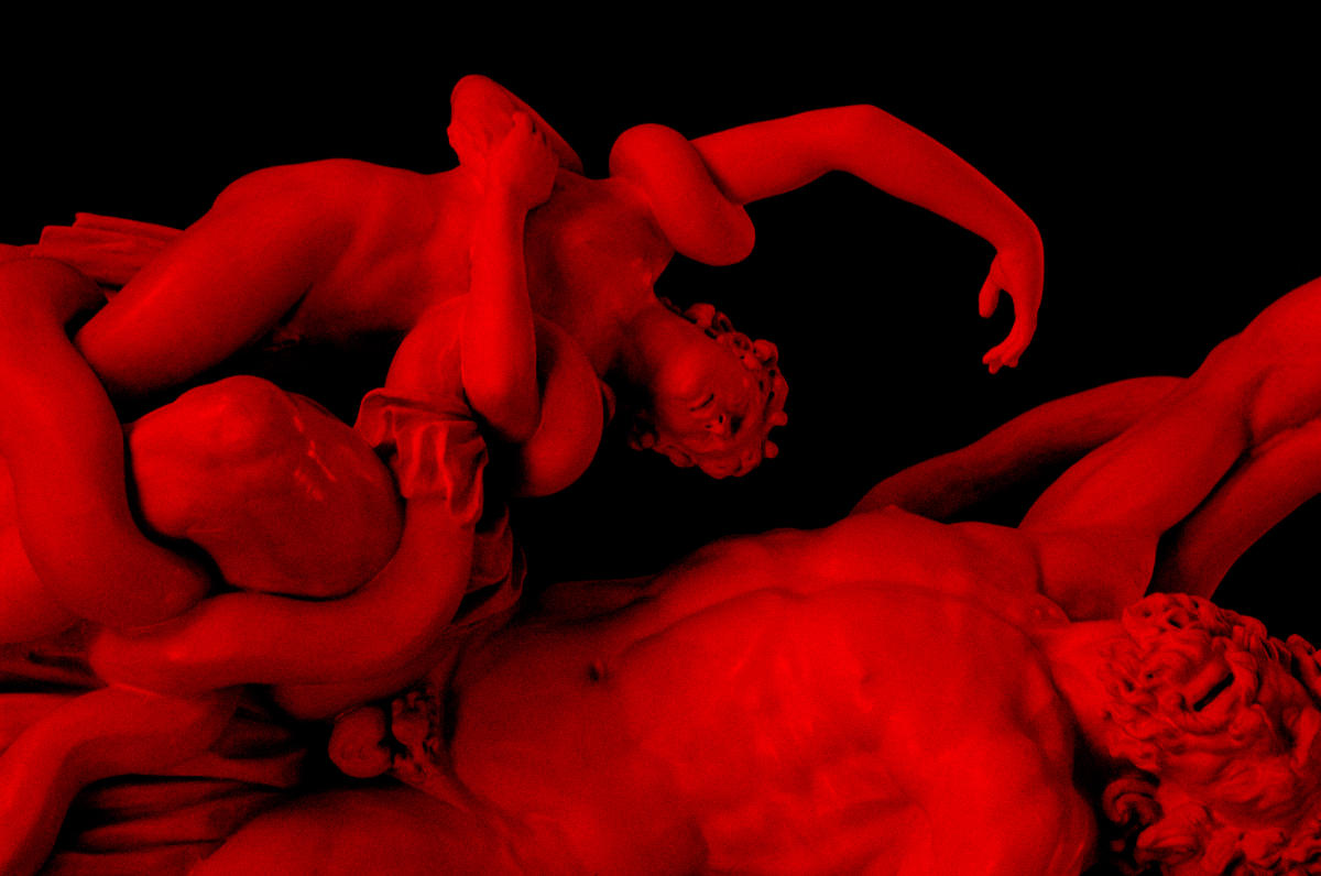 Brian Teeling and Jennie Taylor: in the glow of a frozen flame | Friday 17 May  – Sunday 21 July 2024 | Crawford Art Gallery | Image: cropped photo of the sculpture ‘Laocoön and His Sons’; the statue is tipped sideways in the photo (not in real life), and what should be white marble or plaster is shades of crimson; we see a son and the father struggling in the grip of a sea monster; unlike the original in the Vatican both figures appear to have complete arms, not truncated ones 