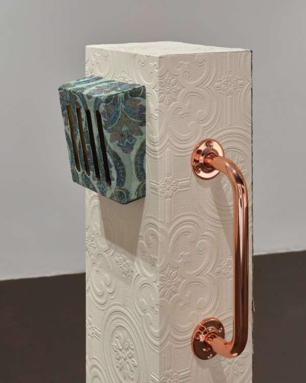 Hazel O’ Sullivan: Retrofuture | Friday 24 May  – Tuesday 11 June 2024 | The LAB | Image: photo of what looks like a truncated concrete post, square in cross-section; it is covered by patterned, embossed white wallpaper; there is a very shiny copper handle attached to one side, and a sort of speaker device (?) covered by a blue-ish wallpaper pattern attached to a second side 