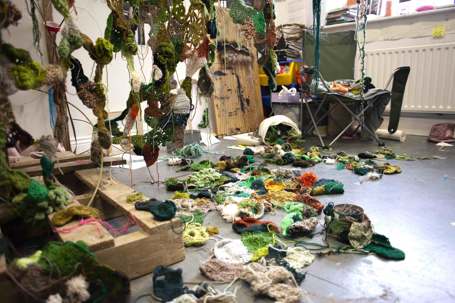 Sarah Holden | Aiteall – fine spell between two clouds | Friday 17 May  – Wednesday 5 June 2024 | Wexford Arts Centre | Image: Sarah Holden | in what may be the artist’s workspace at college, we see what seem to be crocheted objects everywhere – suspended in space, strewn on the floor, on the seat of a folding chair; their colours are organic – greens, yellows, one or two more orange, a few white 
