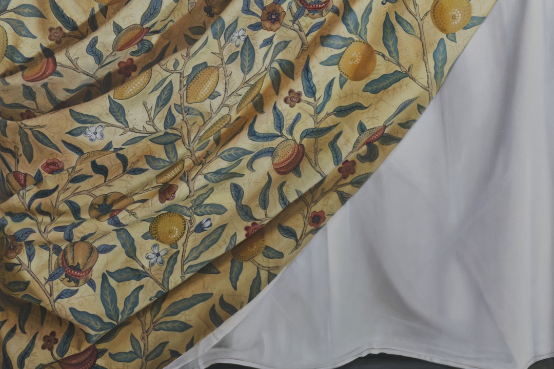 Detail of Jennifer Trouton’s The Last Supper (2023). Photo by Simon Mills, courtesy of the artist. | Ursula Burke, Joy Gerrard, and Jennifer Trouton: Other Ghosts | Saturday 4 May  – Saturday 29 June 2024 | Ormston House | Image: Detail of Jennifer Trouton’s The Last Supper (2023). Photo by Simon Mills, courtesy of the artist | a rectangular area cropped from the work; we see a patterned cloth sweep from towards top right down towards bottom left; the pattern consists of leaves, twigs (small branches) supporting the leaves, flowers and fruits, and although the leaves seem pretty much the same, the fruits / nuts seem to differ; don’t know what they are; the patterned cloth is in fairly subdued colours, though realistic, with a background colour of pale tan; behind this cloth is another, pure white 