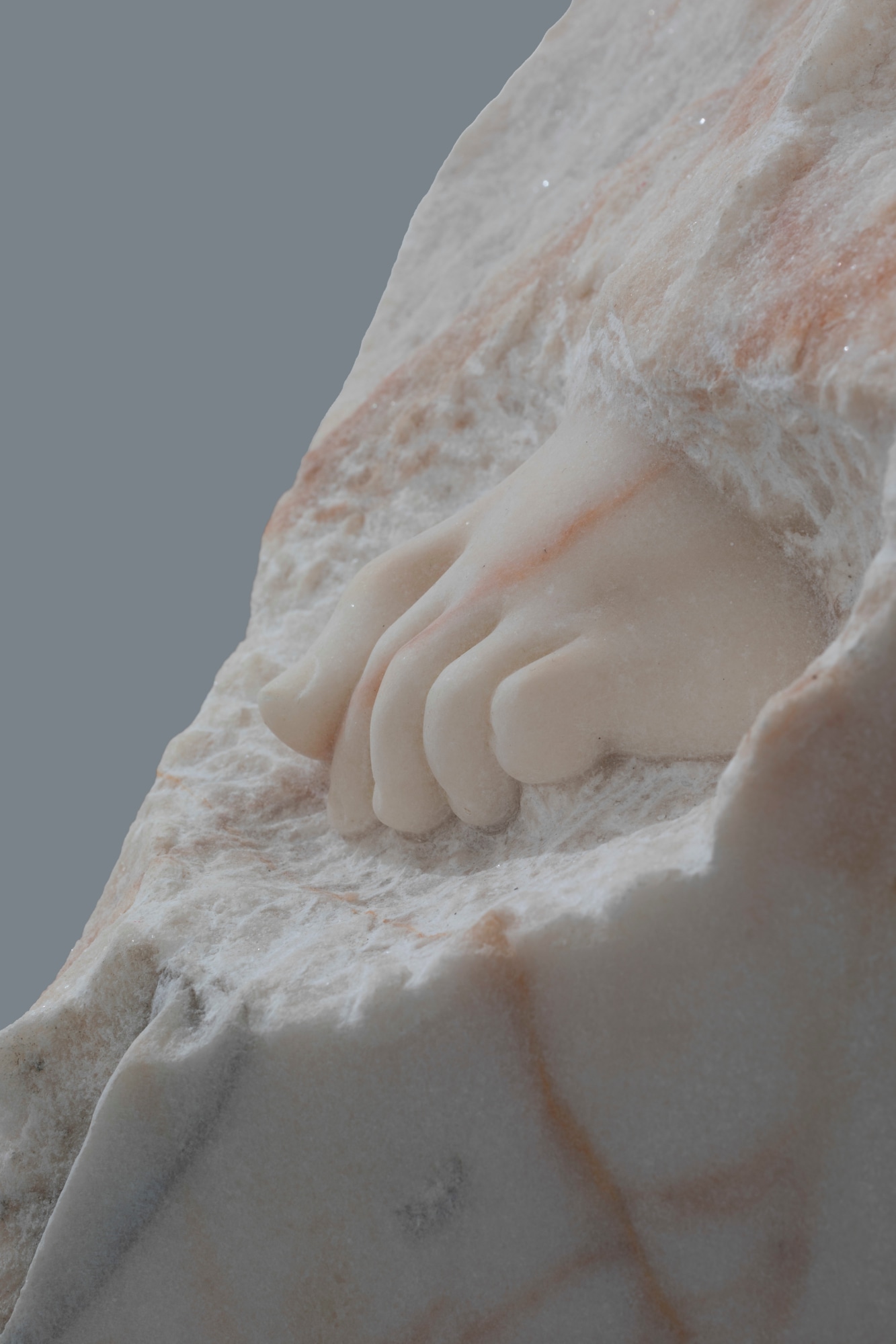 Dorothy Cross: Tread (detail), 2023, hand-carved marble, dimensions variable, https://dnote.website/wp-content/uploads/2024/05/veins-of-other-cross-375x375.jpeg | Dorothy Cross: Veins of Other | Friday 24 May  – Saturday 6 July 2024 | Kerlin Gallery | Image: Dorothy Cross: Tread (detail), 2023, hand-carved marble, dimensions variable | photo of a sculpture in marble; we see not much more than the toes of what may be a child’s foot sticking out of otherwise unchiselled marble; the marble has orange veins running through it 