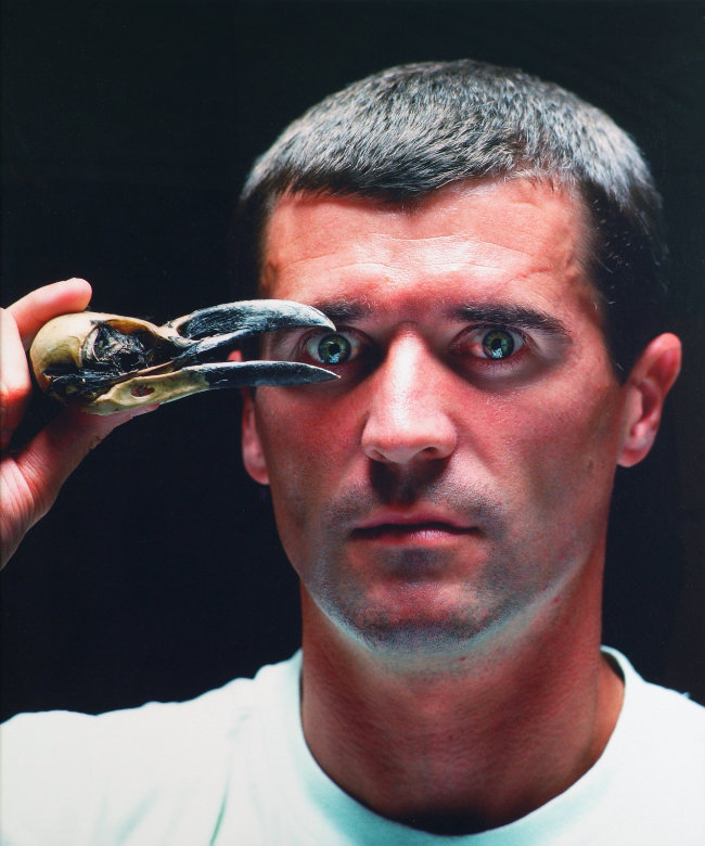 Murdo MacLeod, Portrait of Roy Keane, 2002. © the artist. | NOW YOU SEE IT… | Saturday 20 July  – Sunday 22 September 2024 | Crawford Art Gallery | Image: Murdo MacLeod, Portrait of Roy Keane, 2002. © the artist | close-up photo of the famous Corkonian holding the skull of a bird in his right hand; the beak of the is open, and it is positioned such that you can imagine it holding Keane’s right eye or iris; of Keane we only see the head, a bit of the right shoulder and a bit of the right hand; the background is black 
