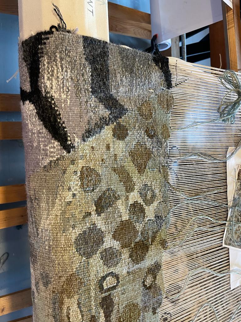 Timelines, Growth and Catastrophe | Saturday 21 September  – Thursday 24 October 2024 | Roscommon Arts Centre | Image: photo of a tapestry on a loom (?); the photo appears to be rotated by 90º; to the right we see thick strands into which there is nothing yet woven, and towards the left we see the emerging tapestry, which of organic shapes, mostly round-ish, in earthy tones against a paler, fairly randomly patterned background 