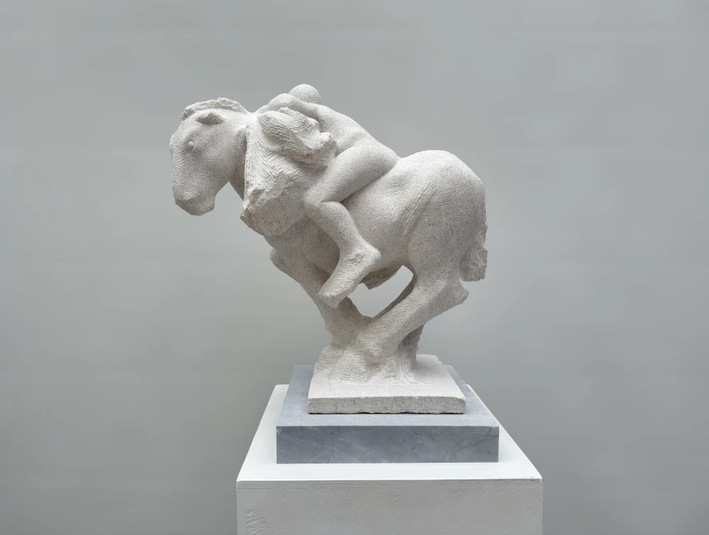 Michael Quane: Our Belongings, Nabresina Light Limestone, 2024, 62 x 48 x 23 cm | Michael Quane RHA: Belonging | Thursday 26 September  – Saturday 19 October 2024 | Solomon Fine Art | Image: Our Belongings, Nabresina Light Limestone, 2024, 62 x 48 x 23 cm | photo of a white-ish, fairly representational sculpture on a plinth; the view is from the side; we see a figure on a horse which is possibly galloping; some large package seems to be between the figure and the mane of the horse – possibly the ‘belongings’ of the title 