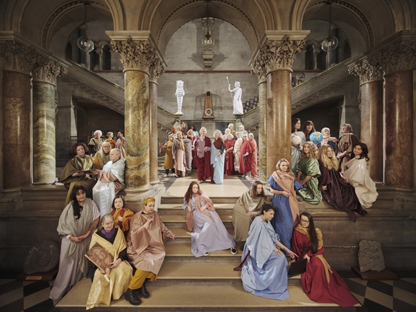 Na Cailleacha: The School of Hibernia (after Raphael) | Friday 1 November  – Saturday 9 November 2024 | Uillinn: West Cork Arts Centre | Image: photograph; very classical / Renaissance architecture with lots of shining marble; at the back, stairways descend to a landing in the centre of the sceneand then down to ta large hallway, from which a stairway leads down towards us; this is a photo containing perhaps 40 figures in classical robes; the show’s text elucidates: “…an all-women cast is set in the Museum Building of Trinity College Dublin. This image features forty-one contemporary Irish women from a variety of age profiles and backgrounds, all leaders in their fields, who have contributed to human knowledge.” 