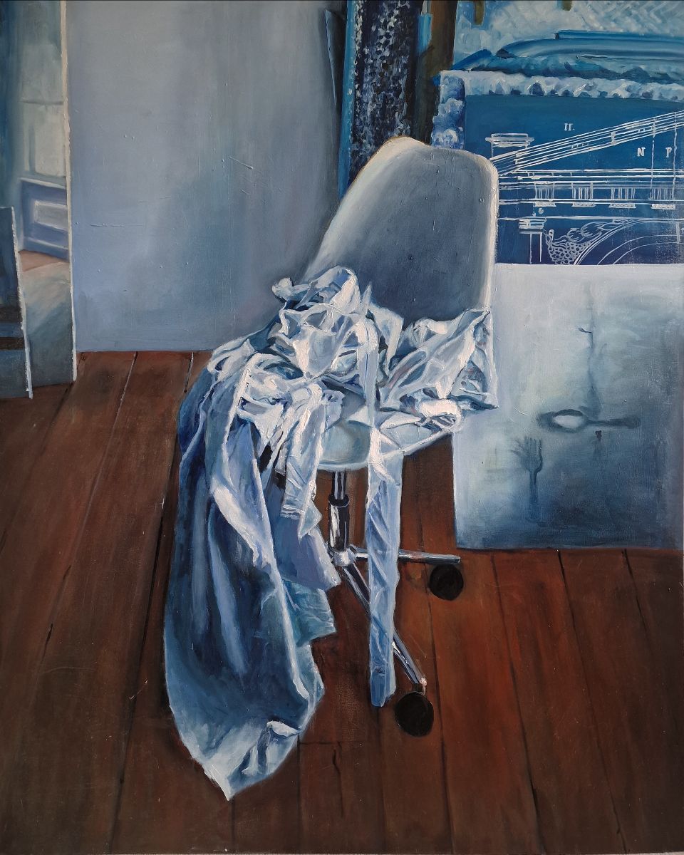 Mary Kelly: He couldn’t find her, oil on canvas, 100 x 120cm | Mary Kelly: Unlimited | Saturday 26 October  – Saturday 16 November 2024 |  | Image: Mary Kelly: He couldn’t find her, oil on canvas, 100 x 120cm | the painting is dominated by an office chair – one on wheels – on which we see a pile of clothing, some of which hangs down the floor; both chair and clothing and, indeed, the canvases we see behind the chair, are all in muted blues and greys; the floor is wood, and ruddy-red 