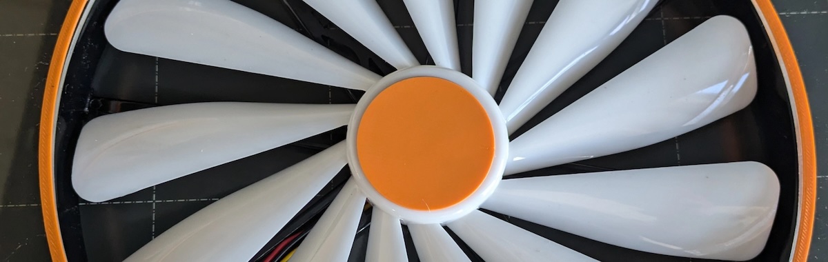 Adam Gibney: Cybernetic Reorientations of Being: NOVA | Saturday 7 December 2024  – Saturday 8 February 2025 | Mermaid Arts Centre | Image: photo, probably of a detail of one of Gibney’s works; it looks like the sort of propellor you might find in a cooling fan of some electronic object, though it is quite carefully styled – orange, filled circle at the centre point, orange circle around the blades, which are white and shiny 