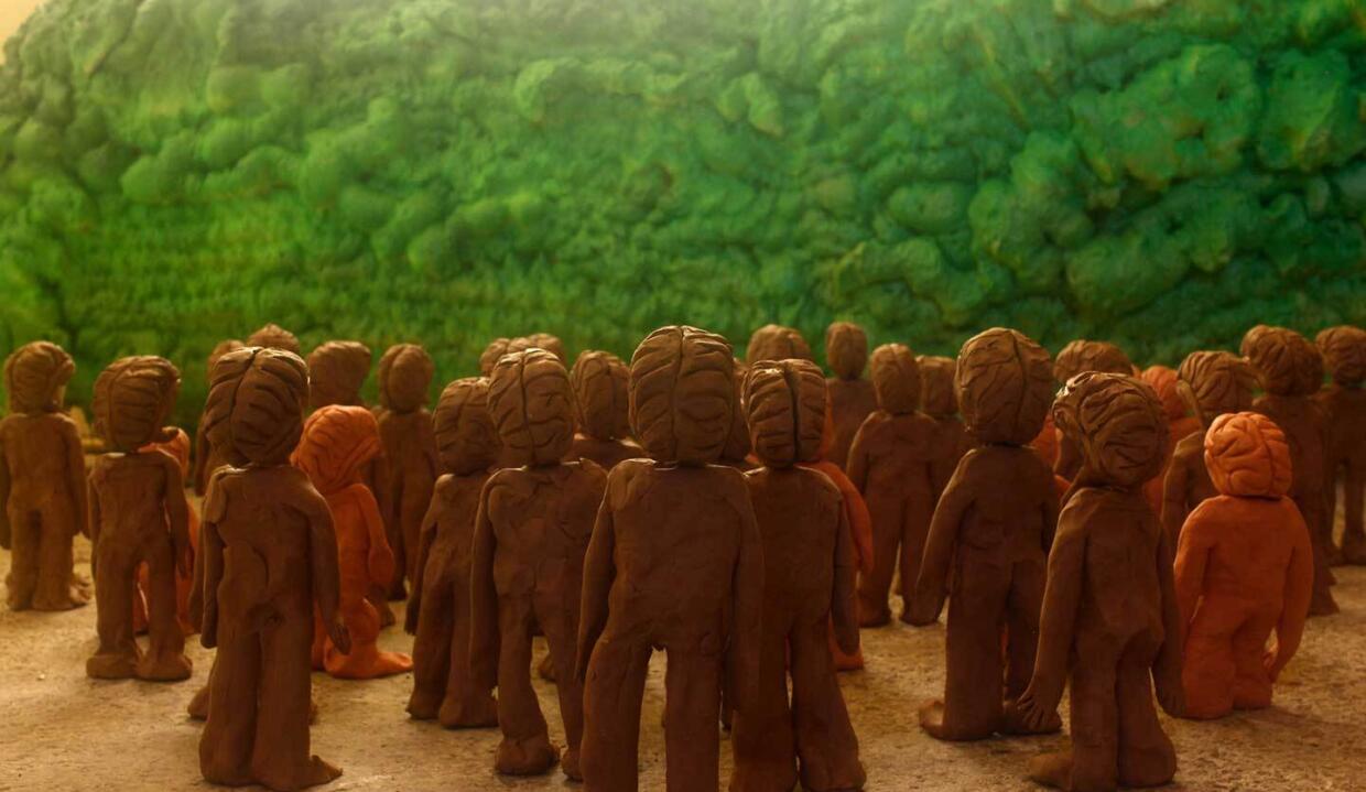 Seiko Hayase: Sun Of Unfortunately | Friday 22 November 2024  – Saturday 25 January 2025 | Rua Red | Image: photo of maybe thirty clay or plasticine figures looking away from us and apparently upwards towards a light source; most of the figures are roughly shaped out of the modelling material, and their heads appear to be brains; some of the figures are a bit smaller and more orange, but most are a mid-brown; they are facing a wall of what looks like green, somewhat randomly knitted wool 