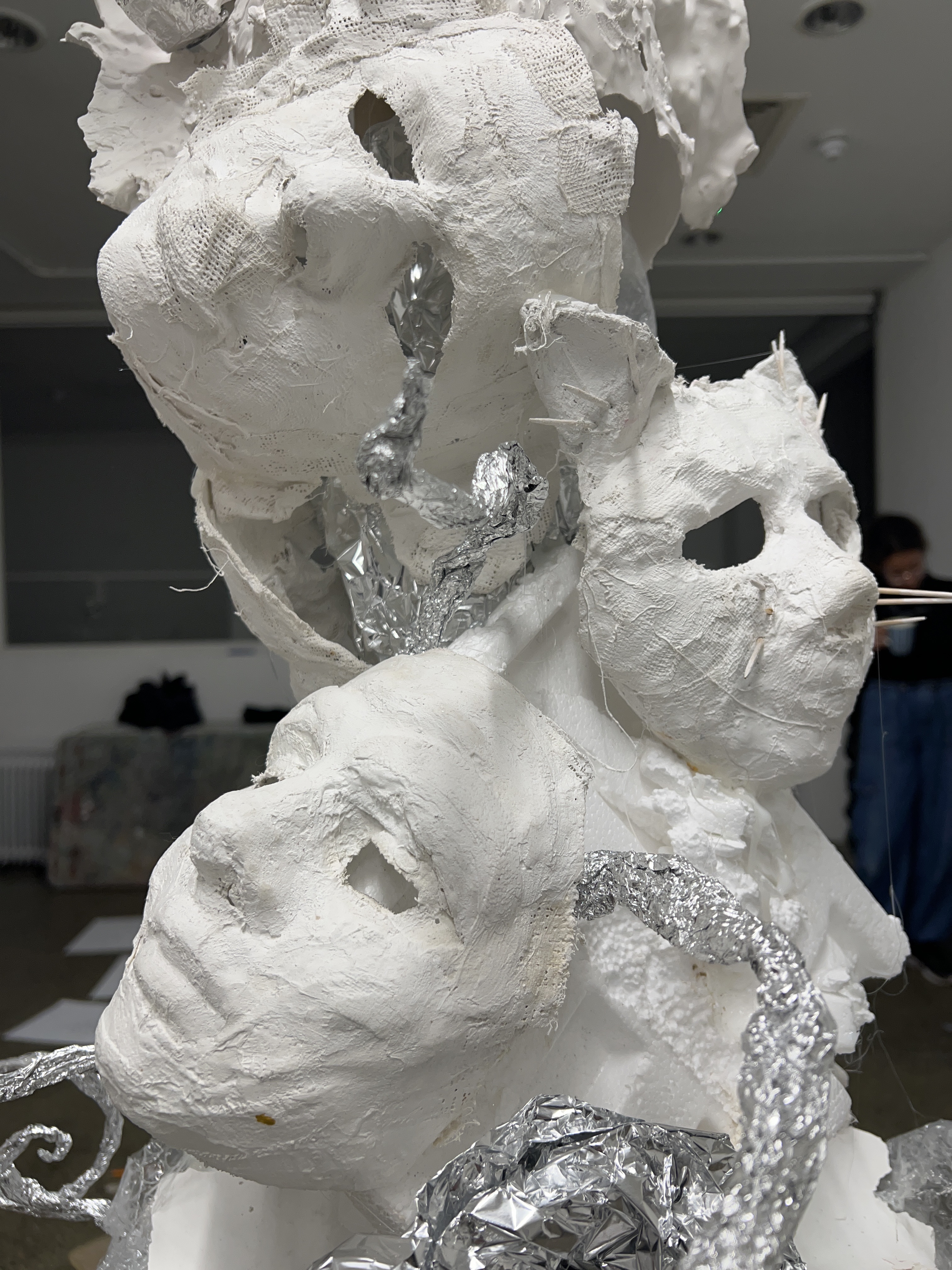 Transformative Power of Art | Saturday 14 December  – Friday 20 December 2024 | Uillinn: West Cork Arts Centre | Image: photo of three white plaster-and-gauze face masks, one above the other; one face is more cat than humana; silver foil twines among the masks; there are probably more masks on the other side of this creation 