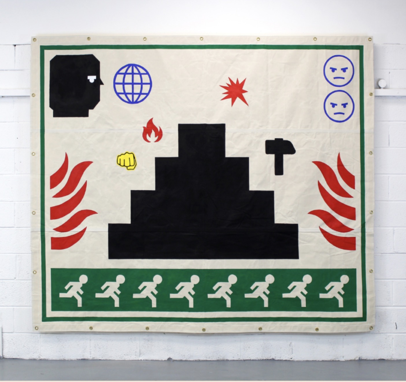 The Project Twins, from Fighting Games | The Project Twins: Fighting Games | Tuesday 25 February  – Saturday 24 May 2025 | Garter Lane Arts Centre | Image: a large, square tarpaulin hanging on a wall; against a creamy-white background we see a design in which green frame surrounds a selection of icon-type images – for example, red flames coming from the left and right, as you might see in a fire warning, and a green band across the bottom with a white figure repeated across it – a running figure heading for an exit (hopefully); top left is what seems to be a blocky black-balaclava-clad head in profile, staring at a smallish wireframe globe, or a small red flash a bit farther across the image, or the two angry-looking simple emoji faces looking at us from the top right corner; there are other small symbols – a yellow fist, a small fire, a black hammer, and in the middle, taking up much room, is a black shape, like a stepped champions podium that could hold seven contestants 