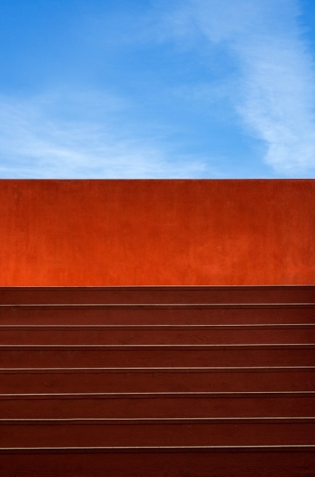 Daniel Holfeld, Infinite Horizons, 2025, UV print on contravision micro-perforated vinyl mounted on to 5mm black acrylic, 200 x 122cm, Image courtesy of the artist. | Daniel Holfeld: Levels | Thursday 27 February  – Sunday 23 March 2025 | Royal Hibernian Academy | Image: Daniel Holfeld, Infinite Horizons, 2025, UV print on contravision micro-perforated vinyl mounted on to 5mm black acrylic, 200 x 122cm, Image courtesy of the artist | in this photo we appear to be looking at steps straight ahead, going up to a blank wall, illuminated from below; the steps are darker, perhaps made from cedar, while the wall looks more like rusted iron; behind the wall we see blue sky with some cirrus clouds 