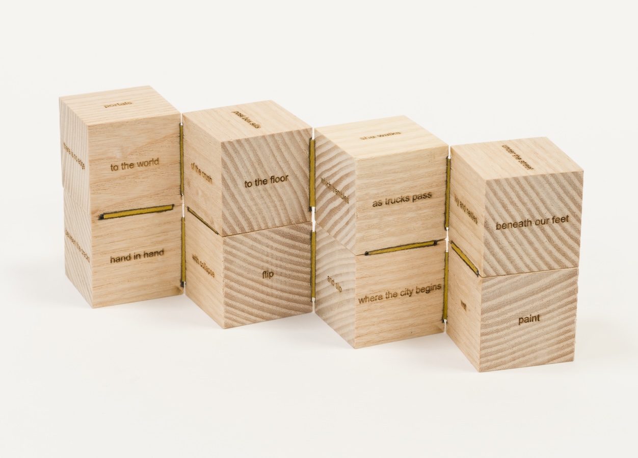 Cristín Leach, To the Line, 2023, wooden sculpture, 6 x 6 x 6cm | Connections | Saturday 8 February  – Sunday 6 April 2025 | Luan Gallery | Image: Cristín Leach, To the Line, 2023, wooden sculpture, 6 x 6 x 6cm | a photo of a wooden cube – possibly made of pine – opened out into eight sub-cubes in a double-decker line; each side of the sub-cube has a phrase written on it – e.g., ‘to the world’, ‘hand in hand’, ‘to the floor’, ’flip’, ‘as trucks pass’, ‘where the city begins’; the ground and background are very white, with only minor shadows 