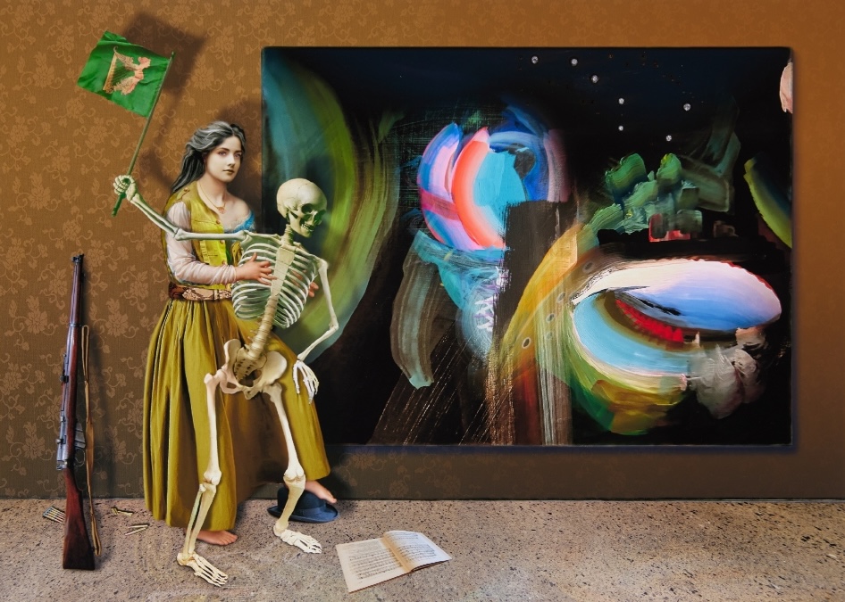 Andrew Folan RHA, The Republic of Pareidolia (abstract entity), 2025, Archival digital print with pyrography and cubic zirconia crystals, 62 x 79cm, Image courtesy of the artist. | 195th RHA Annual Exhibition | Monday 26 May  – Sunday 3 August 2025 | Royal Hibernian Academy | Image: Andrew Folan RHA, The Republic of Pareidolia (abstract entity), 2025, Archival digital print with pyrography and cubic zirconia crystals, 62 x 79cm, Image courtesy of the artist. | complicated image, which is sort of like a photograph – of a painting on a wall which is abstract but only sort-of, a figure towards the left in a long gold dress holding steady a skeleton by the ribs, while it hoists an Irish flag (gold harp on green background) in the air; to their left is a rifle propped against the wall, and lying on the floor is a document and a bowler hat 