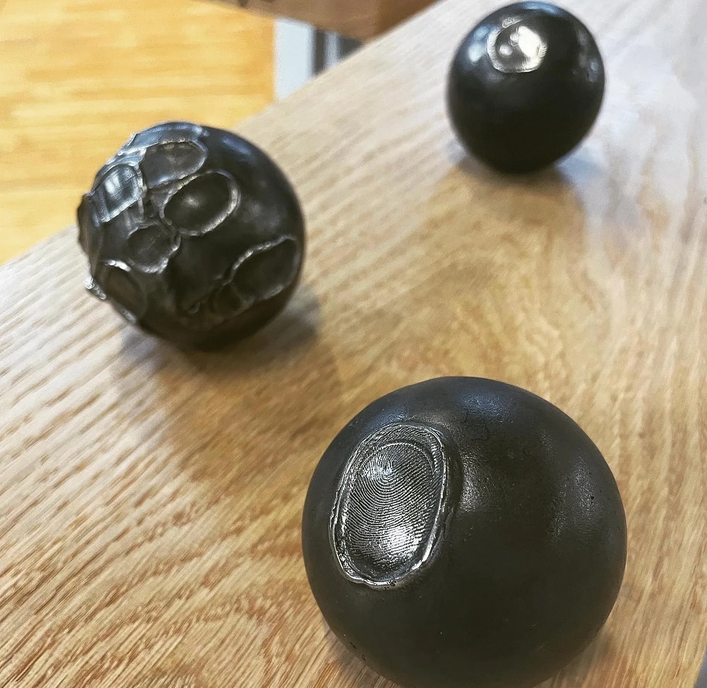 James L Hayes: The Score & Other | Saturday 14 June  – Saturday 19 July 2025 | GOMA Gallery of Modern Art | Image: photo of three balls of – probably – cast iron; each is black and has an impress on its surface; on one the impression seems to include a fingerprint, on another, maybe something to do with the bones of the hand 