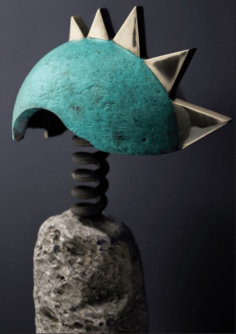Darran McGlynn: Oh What A State | Friday 5 September  – Friday 17 October 2025 | Roscommon Arts Centre | Image: photo of a somewhat anthropomorphic sculpture – a body of stone, a neck of a a spring, and a helmet possibly of bronze – mostly rounded verdigris, but with shiny gold spikes on a central ridge 