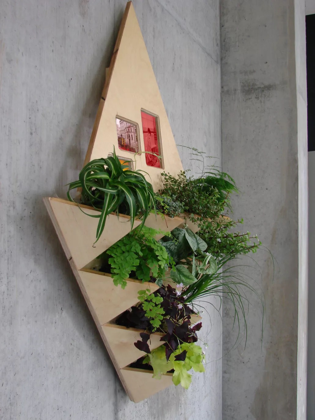 Glenn Loughran: Night Study | Saturday 27 September  – Saturday 25 October 2025 | Uillinn: West Cork Arts Centre | Image: photo; we see two rectangular shapes, cut in ply, one above the other, the top one pointing up, the bottom one down; we’re viewing somewhat from the side; the top triangle appears to have three rounded-corner rectangles cut into it, into which photos have been embedded; the bottom triangle appears to have a total of ten rectangular-shaped ‘pots’ poking out from its surface, also in ply, and each such pot contains a different, presumably live plant (no flowers, just leaves), all healthy 