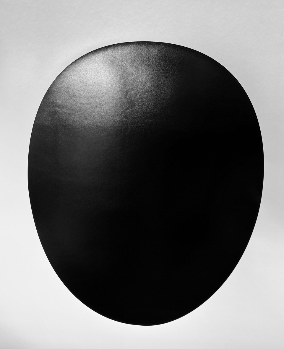 Fergus Martin: Outer Space, 2025; archival pigment print, 160 x 110 cm | Fergus Martin: Space | Friday 26 September  – Friday 31 October 2025 | Green On Red Gallery | Image: Fergus Martin: Outer Space, 2025; archival pigment print, 160 x 110 cm | this appears to be a photo of a print; we see a totally black shape that is like a egg standing on its head – which can more logically be taken as inscrutable but face-like  ro mask-like; there is a sheet off the print such that we can somewhat make out a window in the reflection, and perhaps the shape of the photographer; this is a large print, so the effect must be quite intimidating 