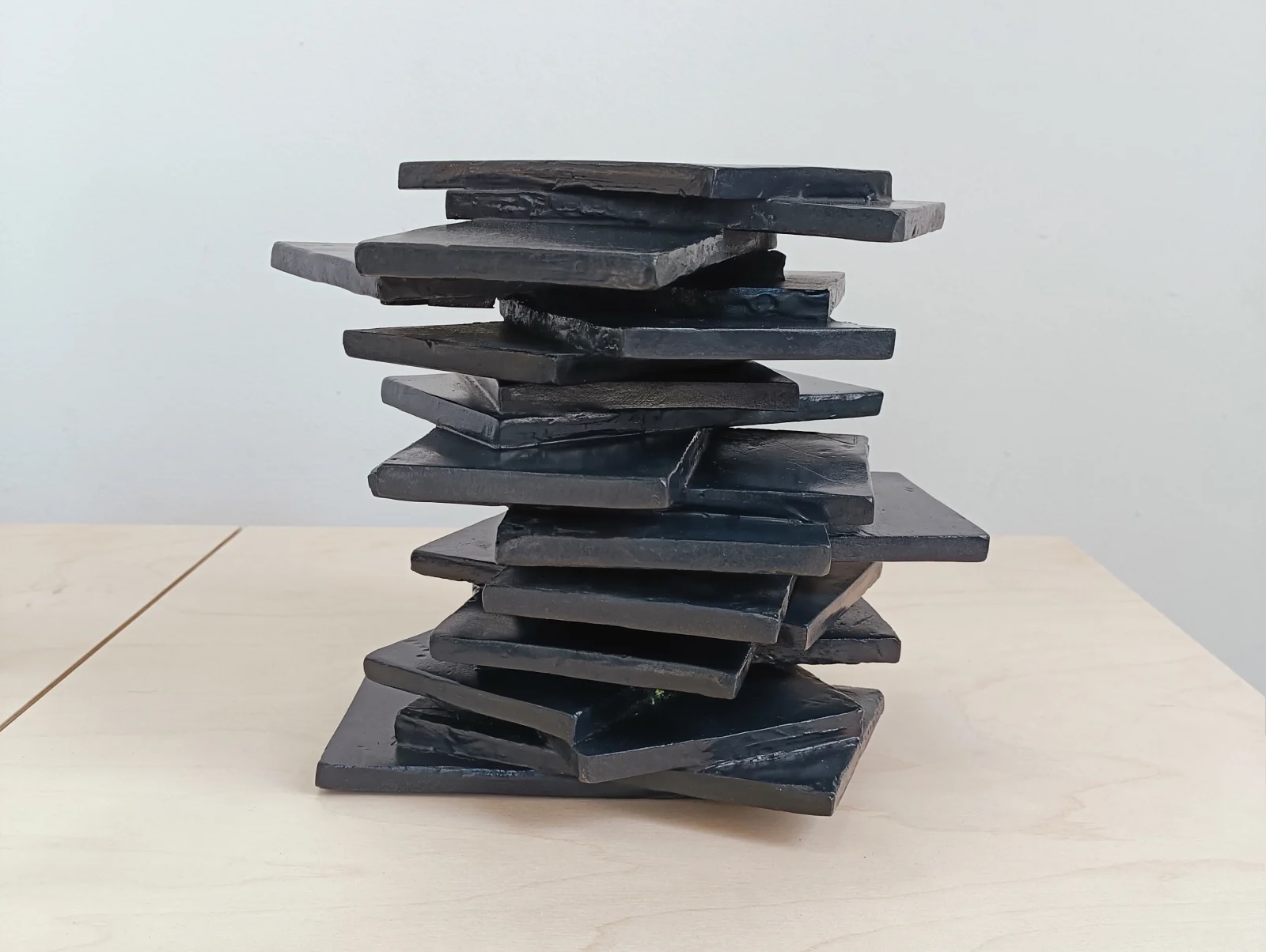 Corban Walker: Untitled (In Less Than One Month), patinated bronze, 20 x 22 x 18 cm | Corban Walker: Resist | Thursday 23 October  – Saturday 15 November 2025 | Solomon Fine Art | Image: Corban Walker: Untitled (In Less Than One Month), patinated bronze, 20 x 22 x 18 cm | photo of a stack of rectangular shapes, roughly comparable to short-ish novels or roof slates; they are patinated dark 