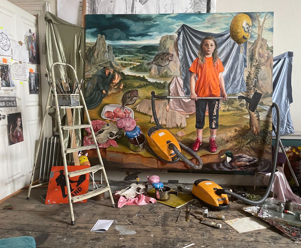 Geraldine O'Neill, Mise en scène, 2025 | Geraldine O’Neill: Flicker, Flicker | Thursday 16 October  – Saturday 15 November 2025 | Kevin Kavanagh | Image: Geraldine O'Neill, Mise en scène, 2025 | this is presumably a photo taken in the artist’s studio; we see a rake of stuff – a step ladder on the left, a vacuum cleaner on the floor, an animal skull on the floor, etc.; on a wall to the left hang various images, possibly source material; facing the camera a very large canvas on which there is a possibly finished painting in a representational style; in it we see a background that is possibly based on a Renaissance painting of saint-in-wilderness variety; there is also a fish or two, a vacuum cleaner, an animal skull, a mallard duck, a Peppa the Pig, a baby on a white tray, a yellow balloon with a face on it…; and in front of a cloth in the painting stands a young figure with long blond hair and a yellow t-shirt holding the vacuum-cleaner shaft thing  