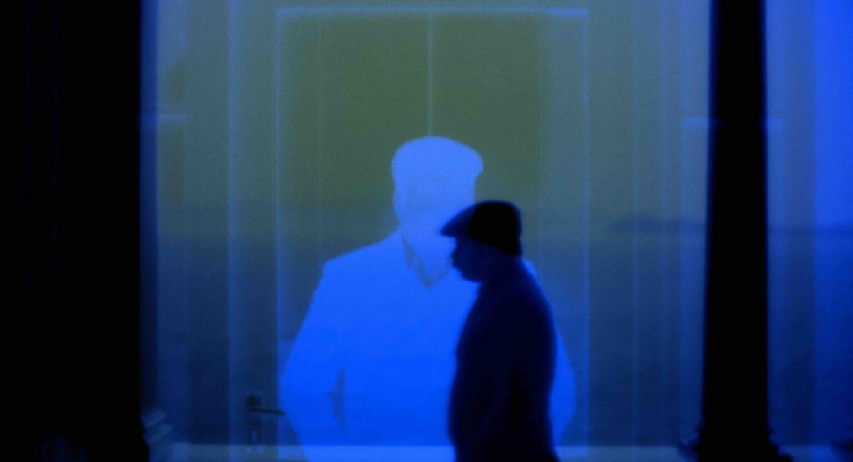 Weird Weird Movie Kids Do Not Watch the Movie (still), 2023 | CineSalon: Worse Things Happen at Sea | Friday 5 December 2025 | SIRIUS | Image: Weird Weird Movie Kids Do Not Watch the Movie (still), 2023 | very blue-ish film still; we see more or less the silouette of the upper body of someone near-centred in the image, wearing a cap, looking due left; ehind this figure there seems to be projected a negative image of the same person, this time looking out towards the camera 