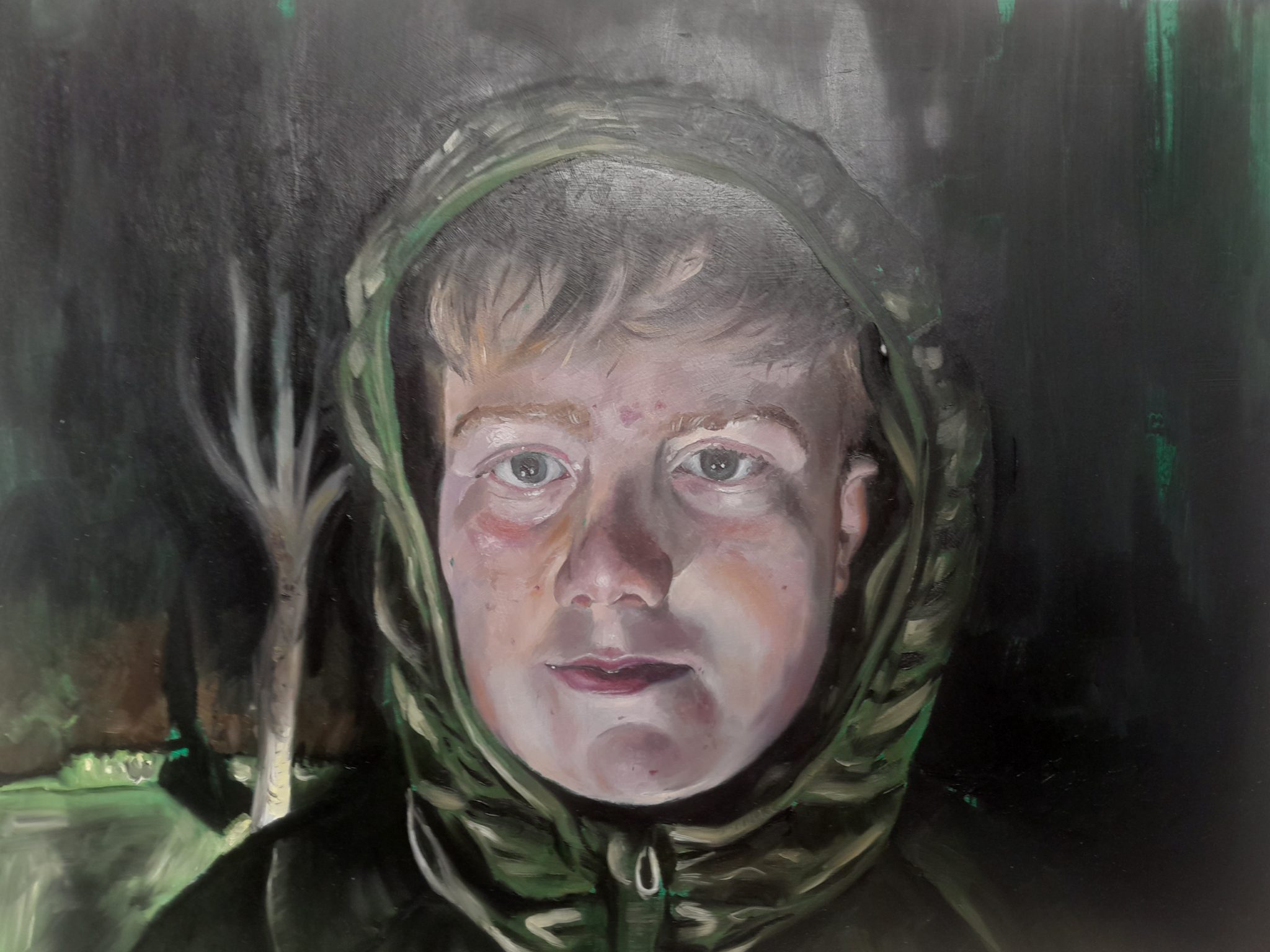 Sean Fitzpatrick, The Boy and the Jade Hour, Oil on Board. | Annual Wexford Lions Club Exhibition 2026 | Saturday 10 January  – Thursday 5 February 2026 | Wexford Arts Centre | Image: Sean Fitzpatrick, The Boy and the Jade Hour, Oil on Board. |  portrait – just the head – of a boy wearing a green hoodie; dark behind, and we seem to see a tree, ghostly, and maybe its shadow; the figure is looinig right at us; pale; lit from below, for the most part 