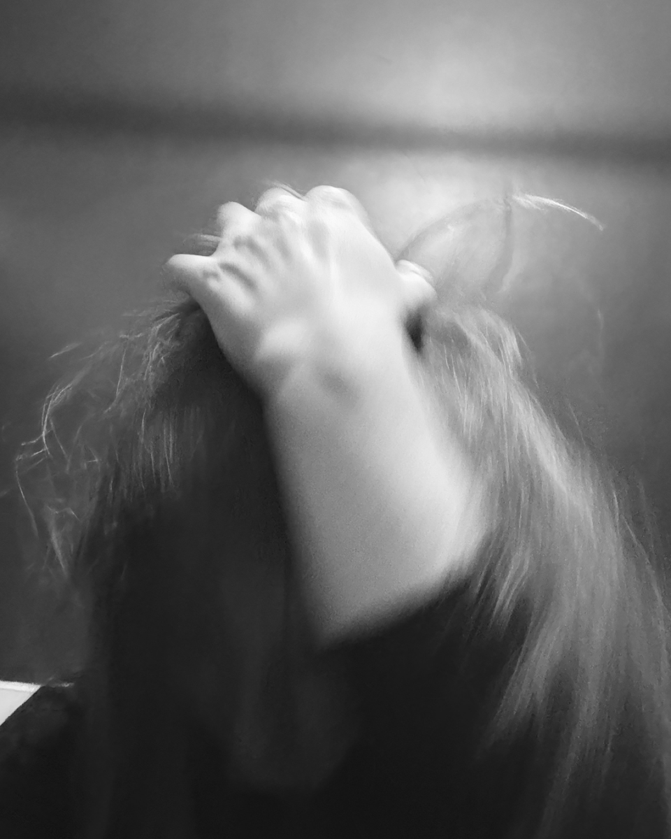 Anna Vidamour, 2026 | Anna Vidamour: ANIMA (The Un-redacted Daughter) | Thursday 7 May  – Tuesday 23 June 2026 | Atypical Gallery | Anna Vidamour, 2026 |  black-and-white photo in which we just see a left forearm, mostly bare, reaching up and grasping the top or back of the head of its owner; we don’t see the face, but we do see much long, fine hair in motion 
