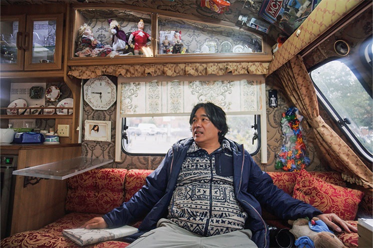 Photo credit: Fenia Kotsopoulou | Shiro Masuyama: The Borderline Project | Monday 1 June  – Sunday 28 June 2026 | Butler Gallery | Image: Photo credit: Fenia Kotsopoulou | we see a figure, presumably the artist, sitting inside an ornately decorated caravan; lots of textiles and textures, dolls, delft 