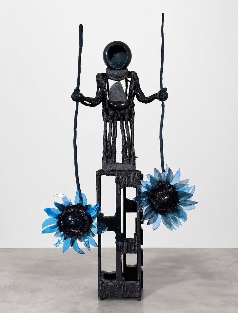 Siobhán Hapaska: The man with a stone in his stomach inverts sunflowers, 2026 aluminium, Jesmonite, wood, epoxy resin 200 × 110 × 85 cm / 78.7 × 43.3 × 33.5 in | Siobhán Hapaska: The Weight of Nothingness | Thursday 4 June  – Saturday 11 July 2026 | Kerlin Gallery | Siobhán Hapaska: The man with a stone in his stomach inverts sunflowers, 2026 aluminium, Jesmonite, wood, epoxy resin 200 × 110 × 85 cm / 78.7 × 43.3 × 33.5 in | photo of a sculpture in a gallery setting; it depicts something like a robot standing on a strange perforated building block while holding in each hand the stem of a sunflower-like flower, though its petals are blue – and the flower-heads are towards the floor, held low rather than high; the head is circular, the chest hollow and holding a rock; the coloration is black, apart from the petals 
